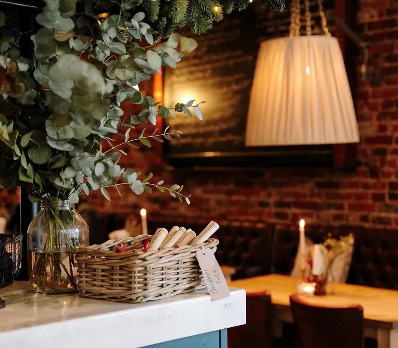 Cosy bar interior with a hanging lamp, exposed brick walls, eucalyptus arrangement and a wicker basket on a marble counter.