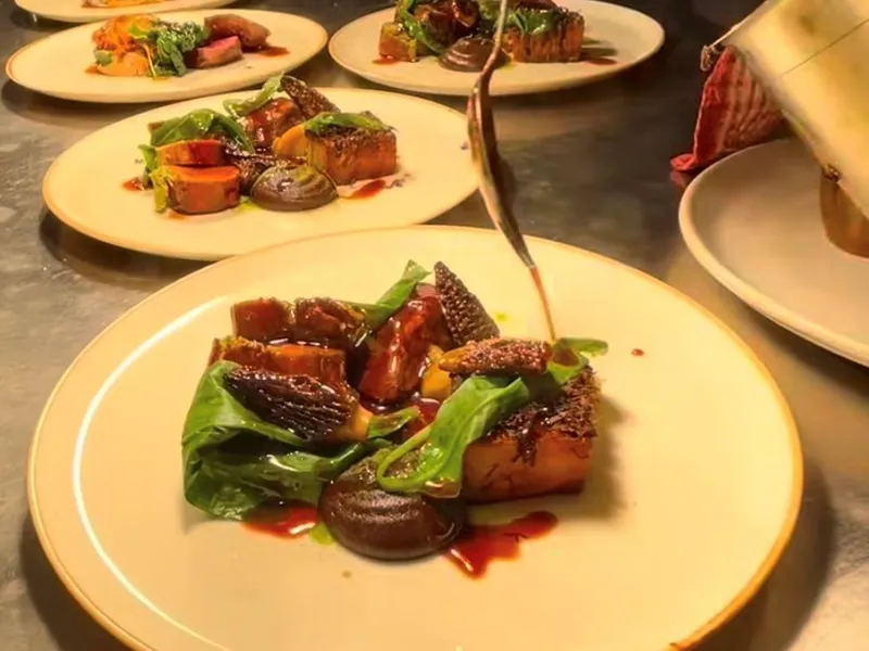 Chef plating gourmet dishes with rich sauce in a professional kitchen pass