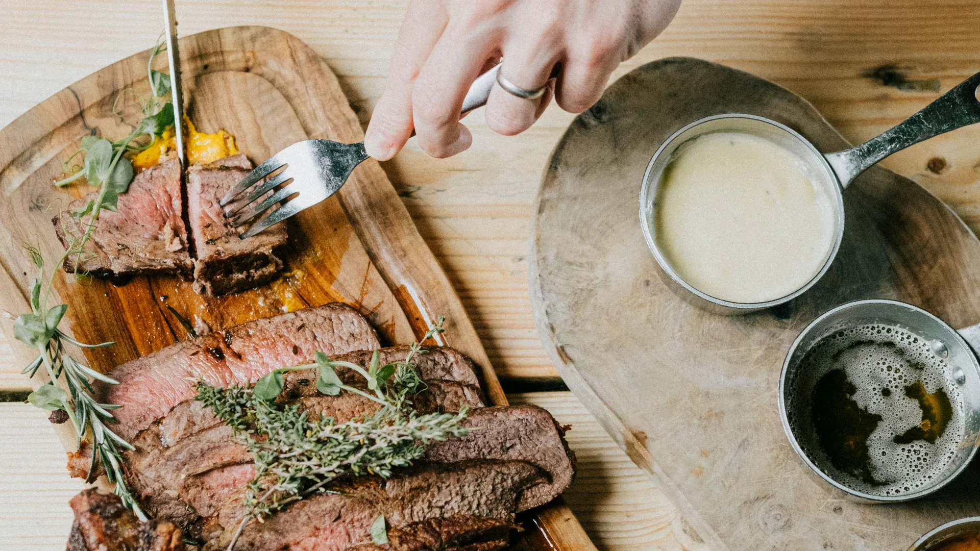 Hands slicing and serving roasted meat on a wooden platter with sauces on a rustic table