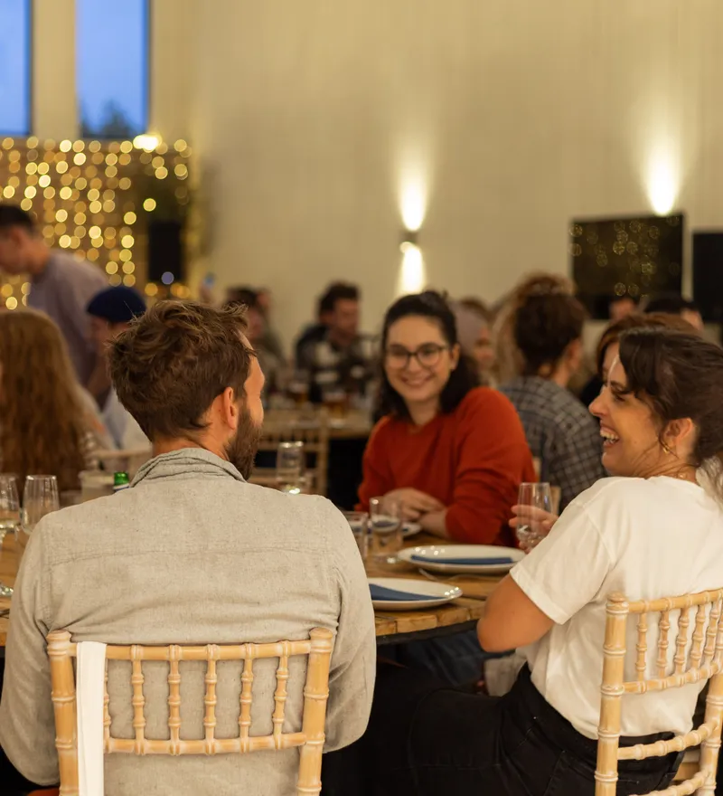 Guests seated around a round table at a corporate dinner event in a warmly lit venue with fairy lights in the background.