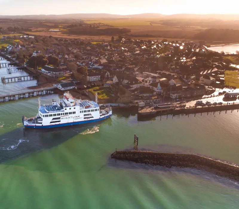 Aerial view of a Wightlink ferry approaching Yarmouth Harbour on the Isle of Wight at sunset.