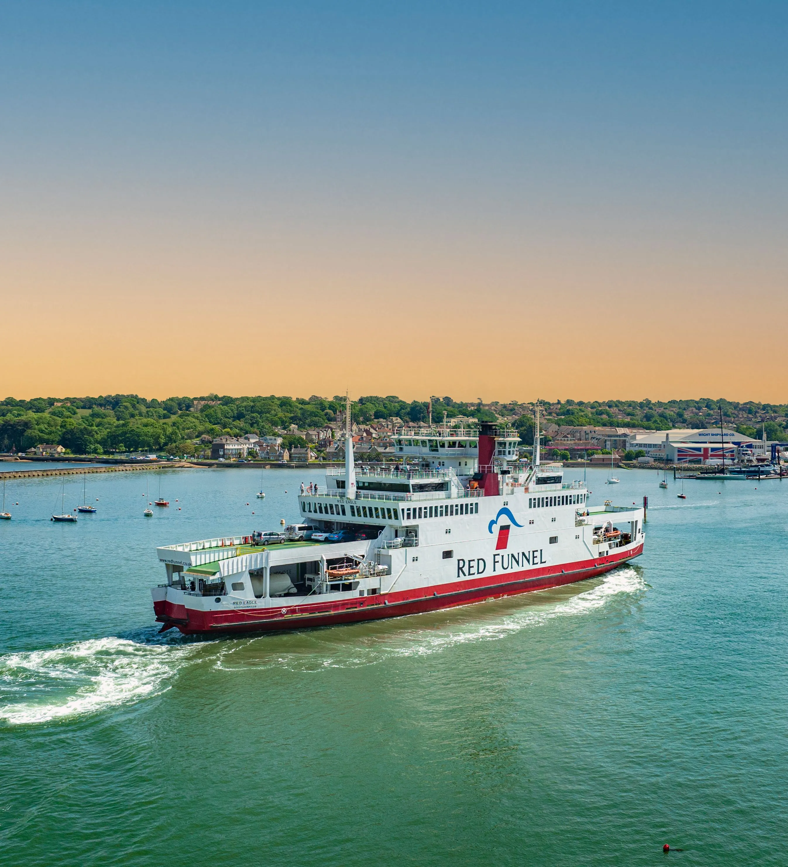 Red Funnel ferry sailing across the harbour at dusk with calm water and a warm evening sky