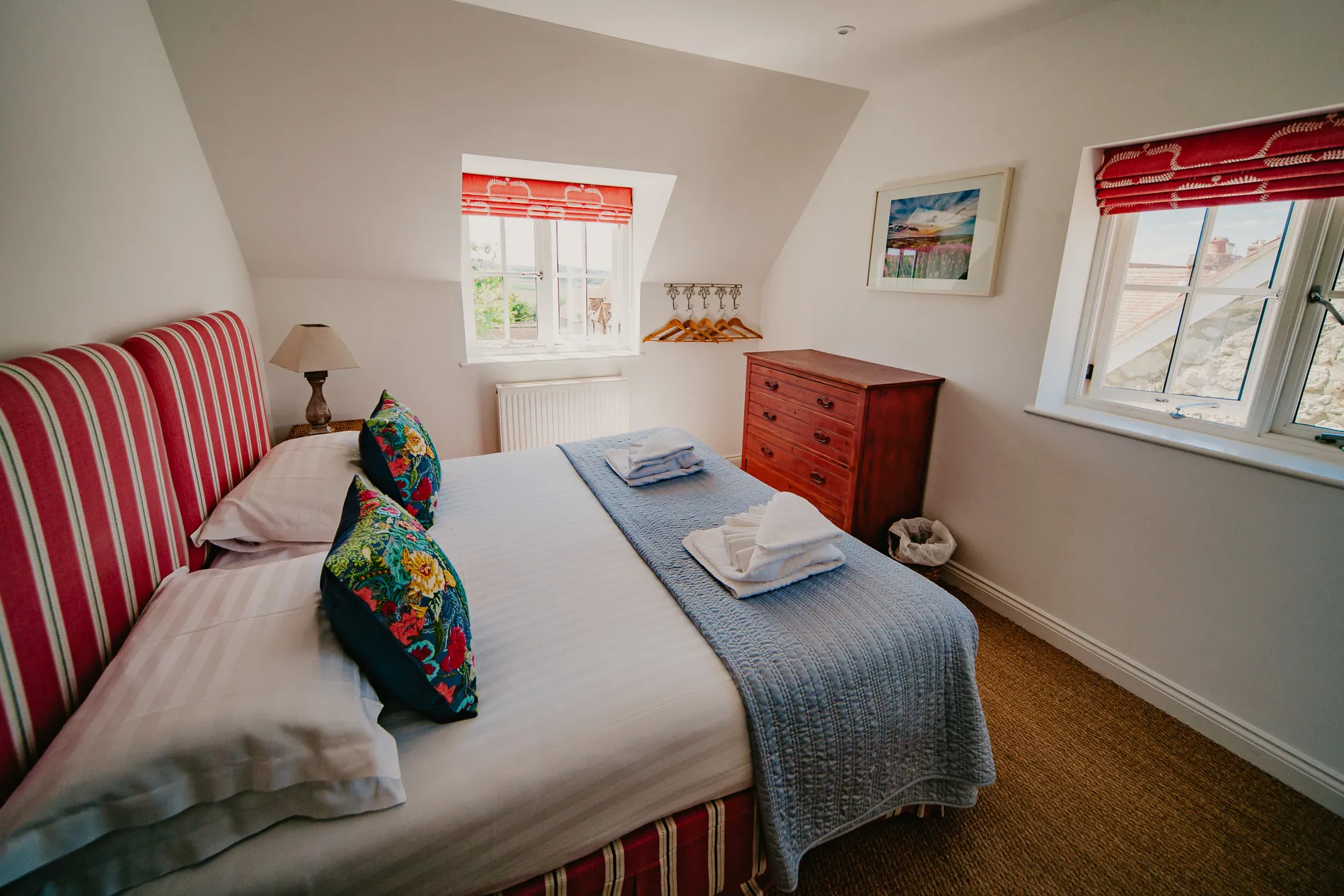 Double bedroom at Dairyman's Cottage, Tapnell Farm with striped headboard, floral cushions and red window blinds