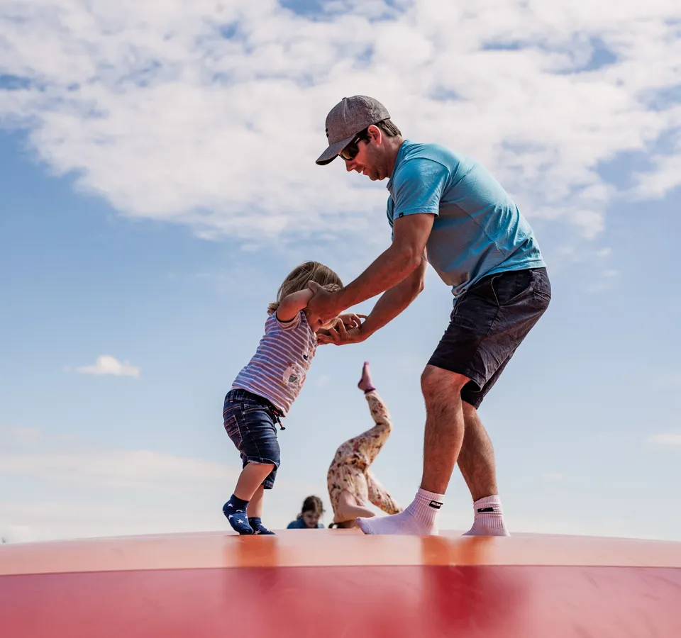 Adult helping a young child bounce on the pillow bounce at Tapnell Farm Park under a bright blue sky