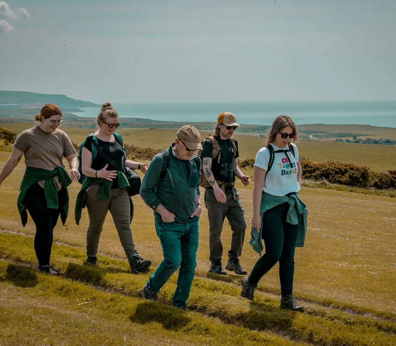 Group of walkers on the Tapnell Farm Wildlife Trail with rolling countryside and sea views in the background