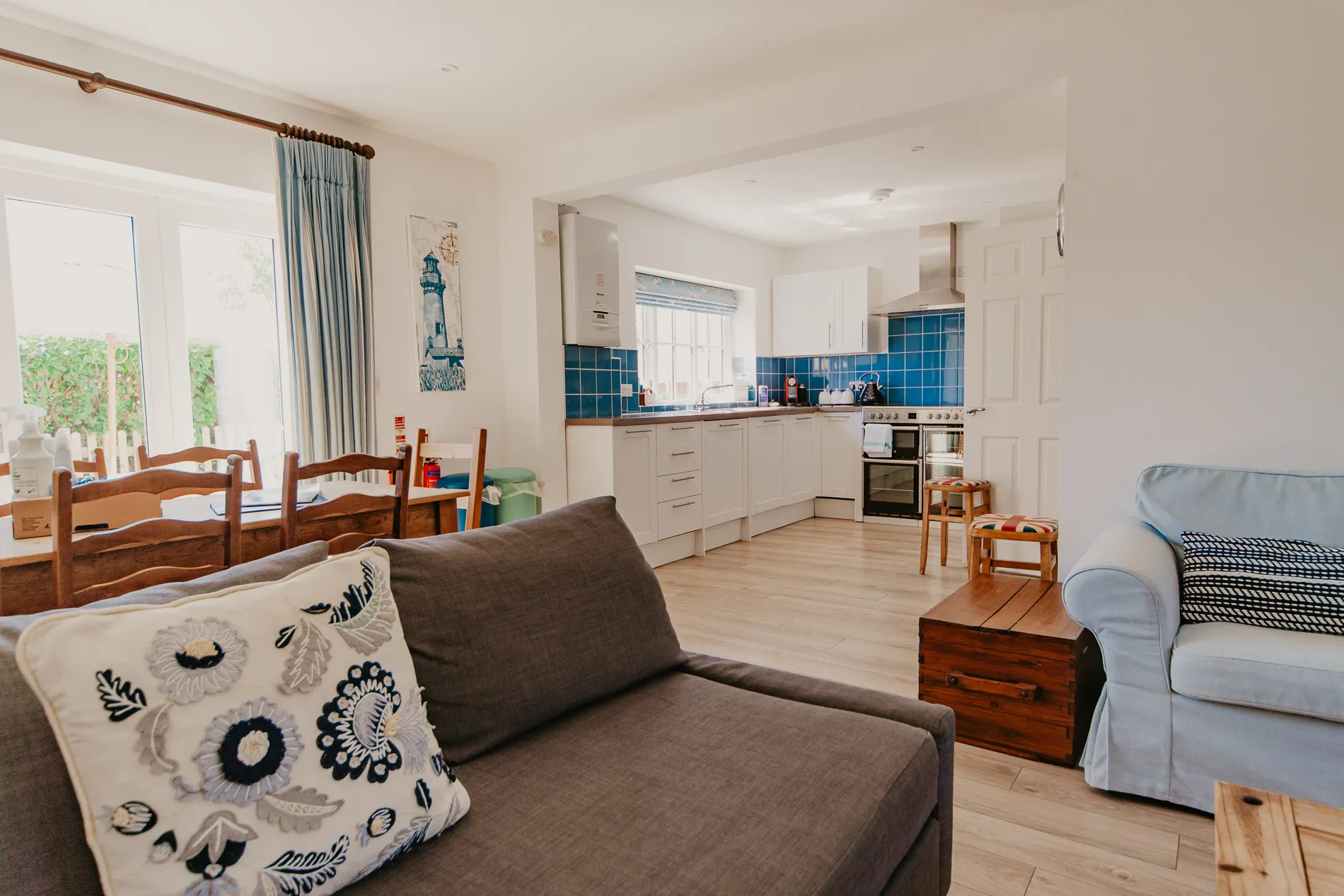 Open plan living area at Dairyman's Cottage, Tapnell Farm, with lounge seating, dining table and white kitchen with blue tiled splashback