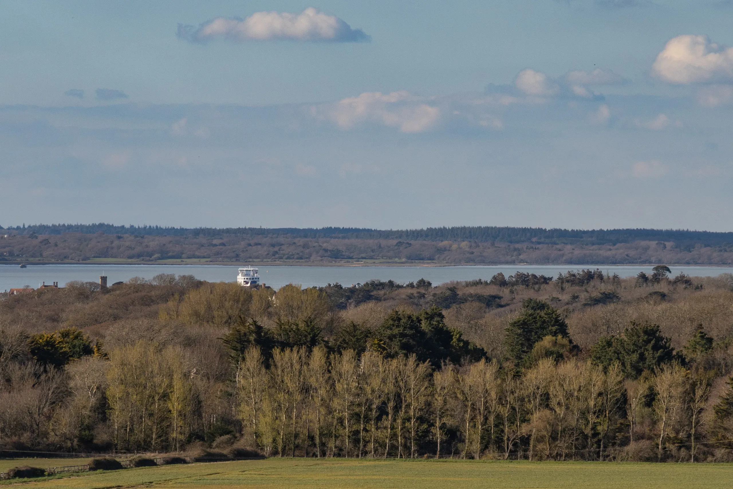 View across woodland and fields towards the Solent on the Isle of Wight under a blue sky with scattered clouds