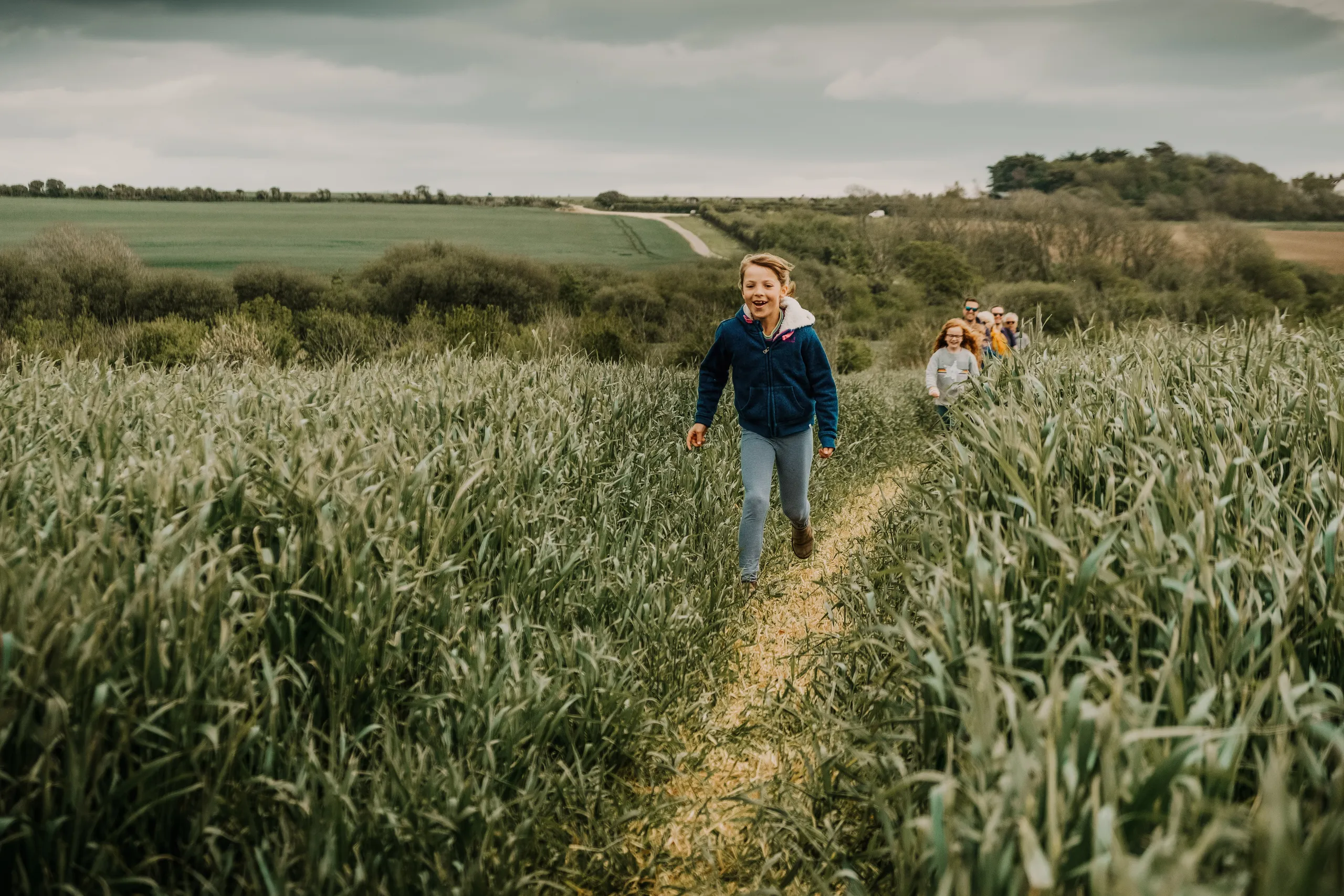 Children and adults exploring the Tapnell Trail through tall green crops at Tapnell Farm.