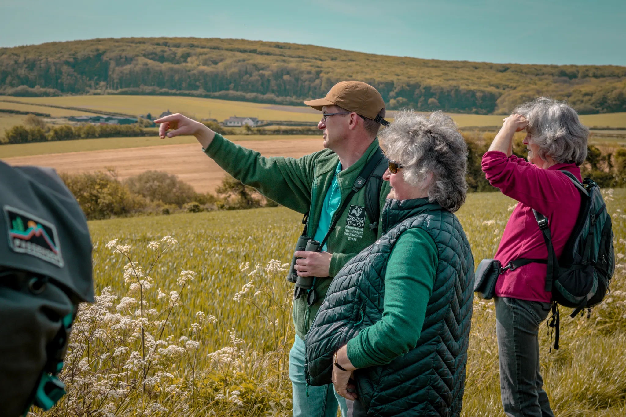 A wildlife guide points across open countryside while leading a small group on the Tapnell Trail.