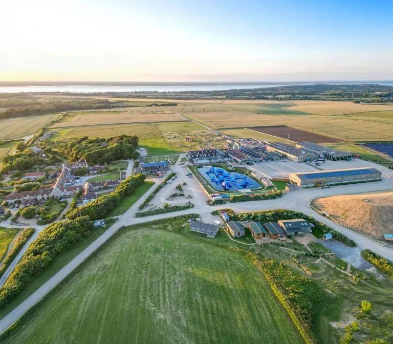 Aerial drone view of Tapnell Farm surrounded by fields and countryside near the coast at sunset.