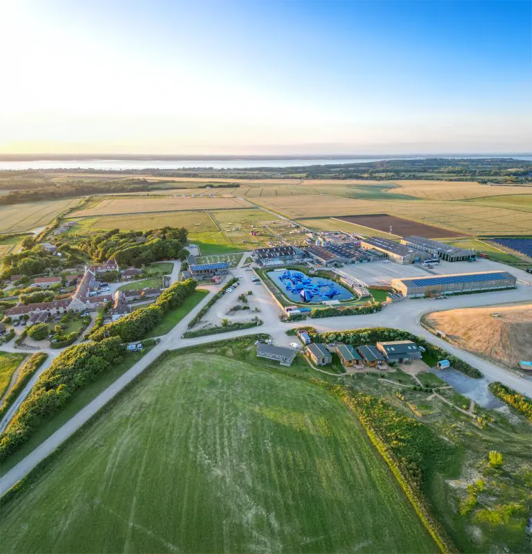 Aerial drone view of Tapnell Farm surrounded by fields and countryside near the coast at sunset.