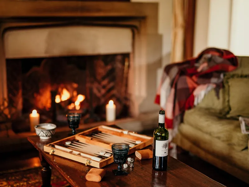 Cosy autumn lounge at Tapnell Manor with a roaring fireplace, candles, a backgammon set and a bottle of wine on a wooden table