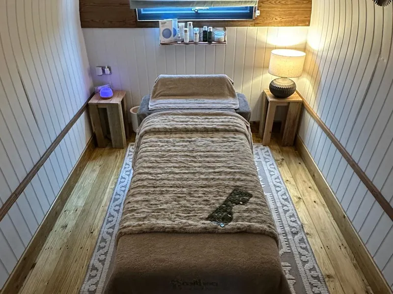 Cosy treatment room with a massage table, wooden floorboards, soft lighting and a patterned rug