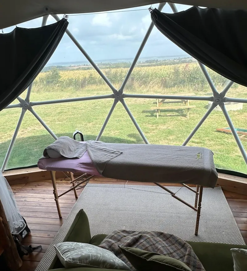 Massage table inside a geodesic dome with countryside views through large windows