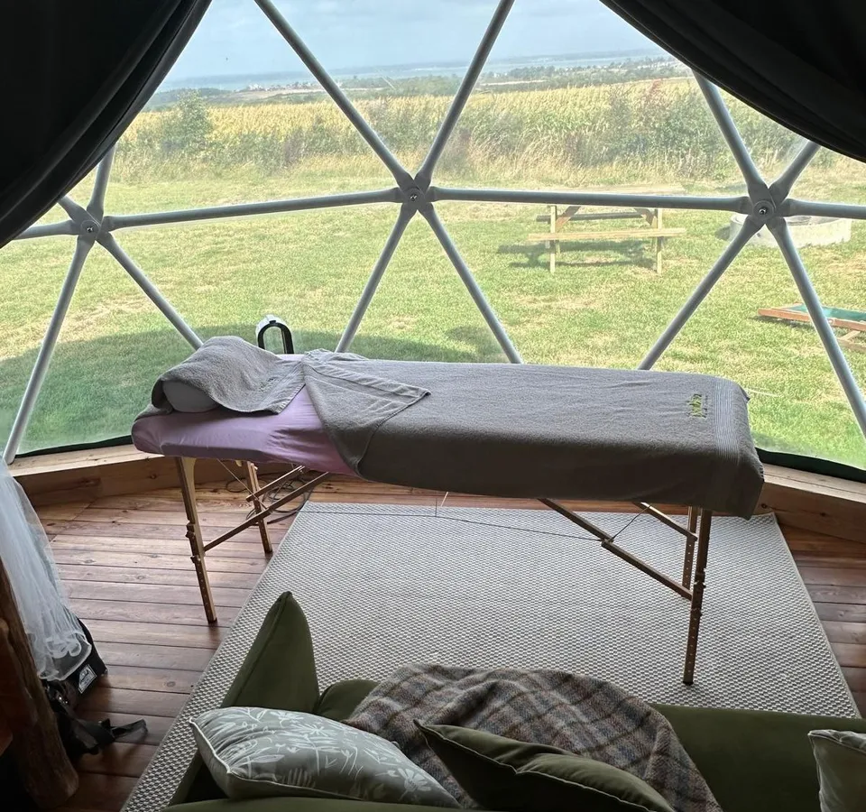 Massage table inside a geodesic dome with countryside views through large windows