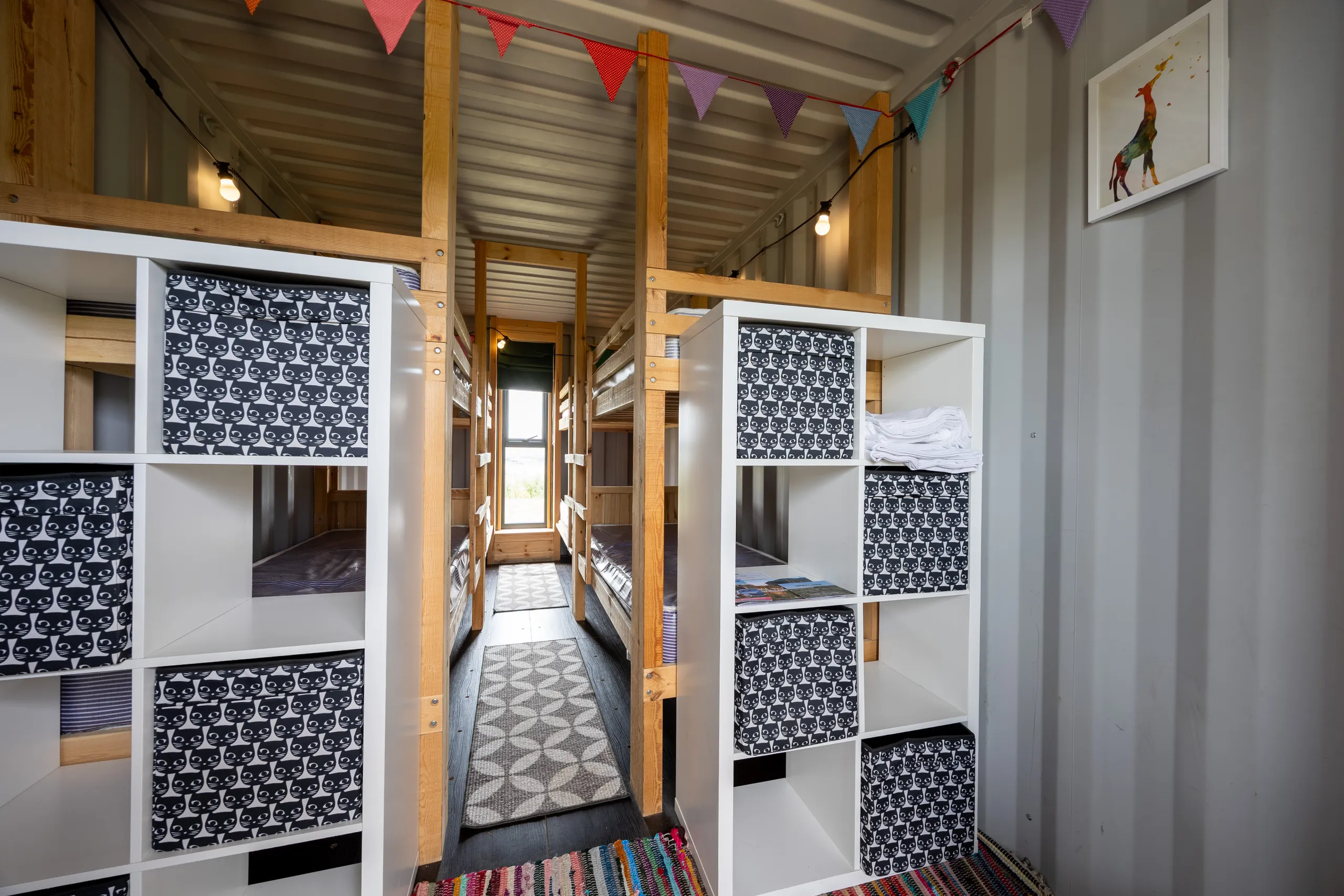 Interior of a bunk room at Tapnell Farm with wooden bunk beds, white shelving, patterned storage boxes and colourful bunting.