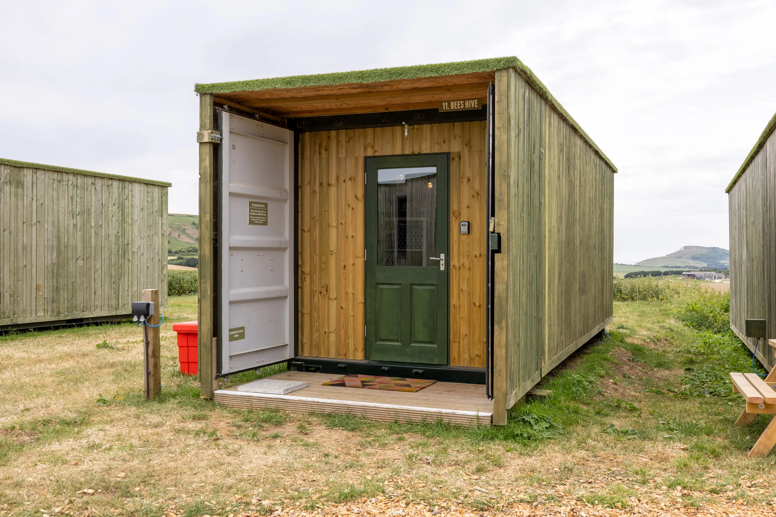 Exterior of the Bees Hive cabin at Tapnell Farm, a timber-clad container-style accommodation unit set in a grassy field with countryside views.