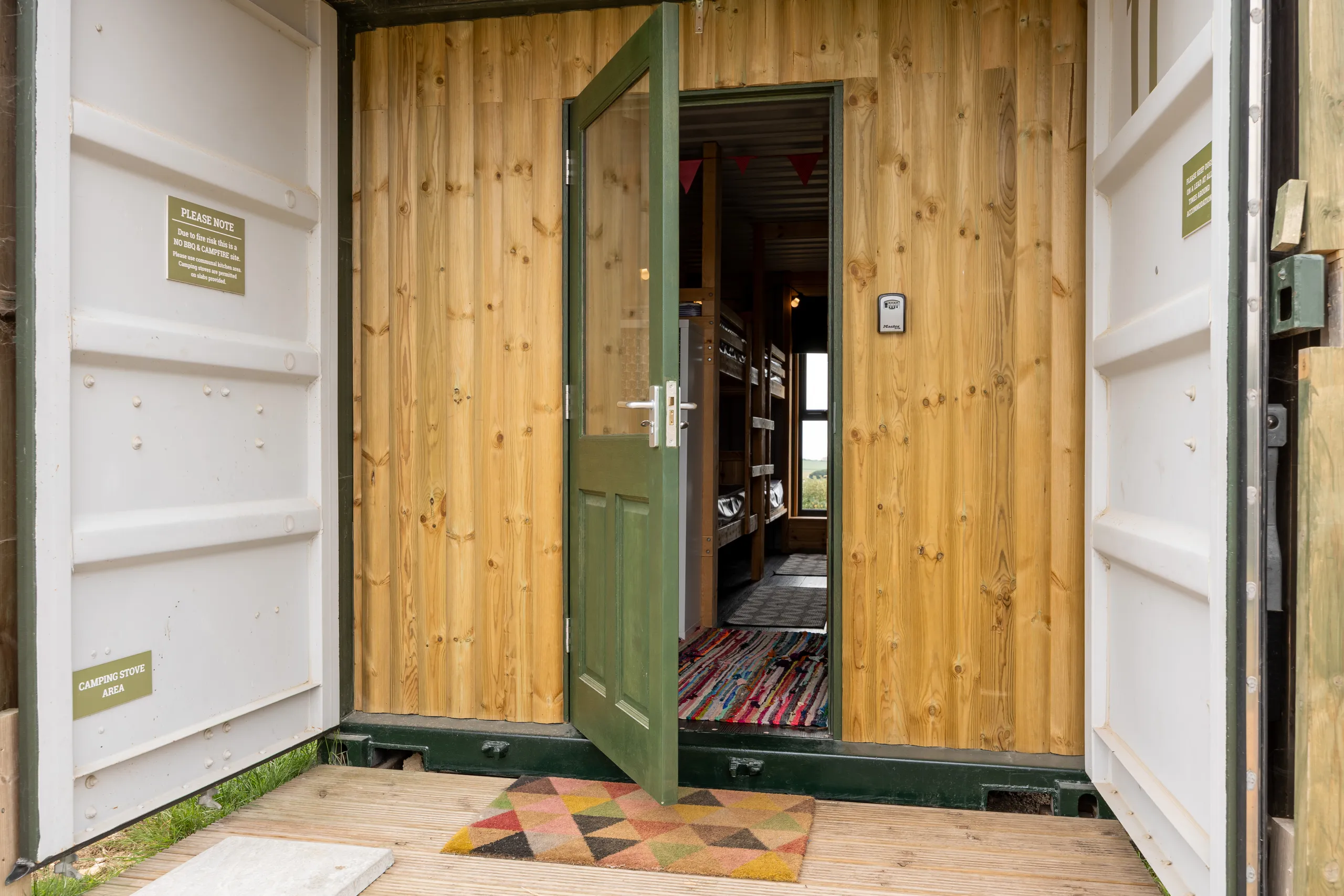 Entrance to a timber-clad glamping cabin at Tapnell Farm with open white container doors and a green door leading to bunk beds inside.