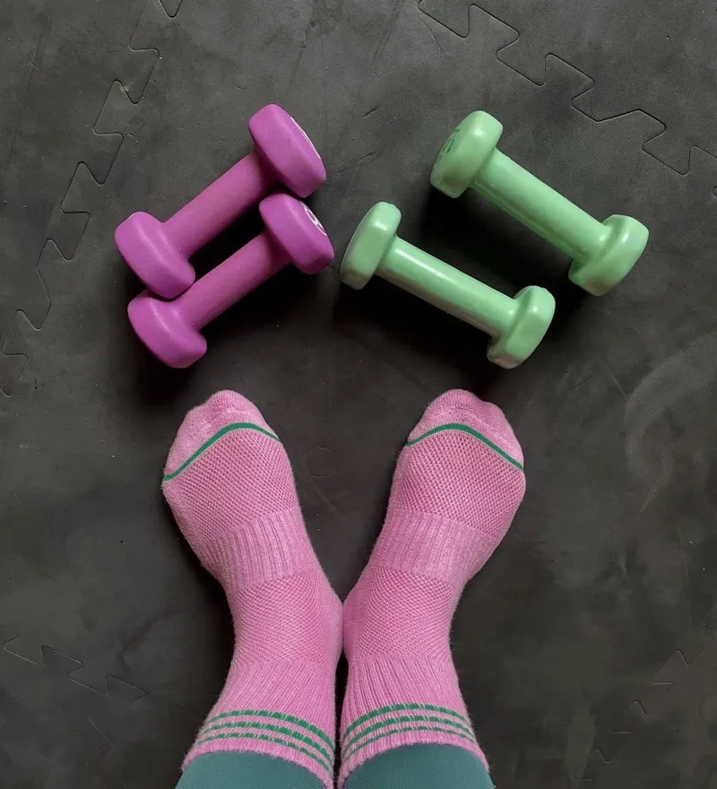 Pink socks and pastel dumbbells on a black exercise mat during a barre workout