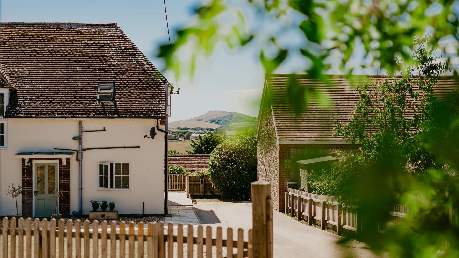 Exterior view of Dairyman's Cottage at Tapnell Farm with a fenced courtyard and countryside hills in the distance