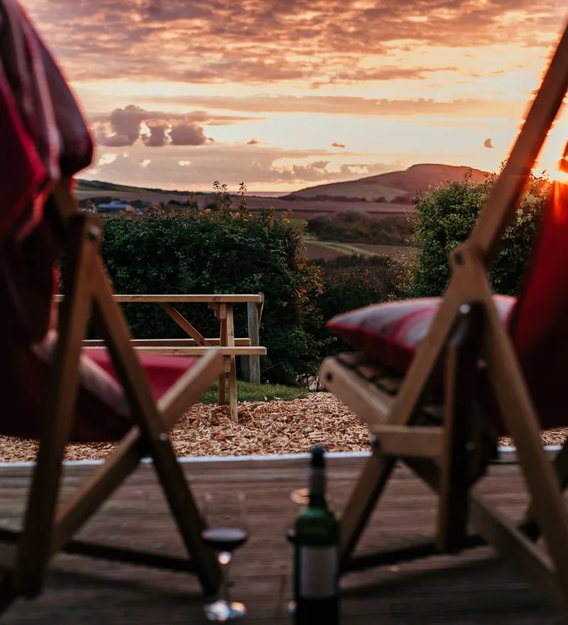 Two deck chairs on the deck of an Eco Pod at Tom's Eco Lodge overlooking a glowing sunset across the countryside.