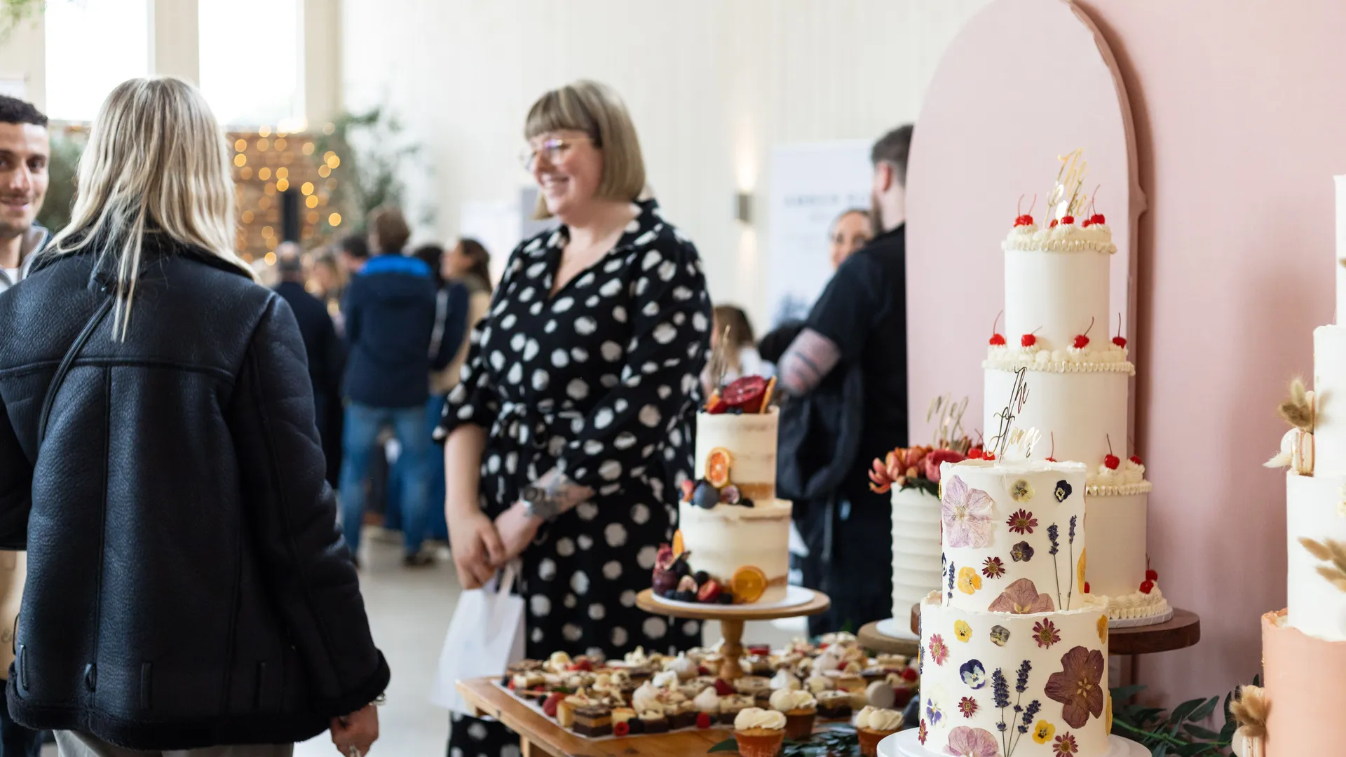 Guests chatting beside a display of wedding cakes and desserts at the East Afton Farmhouse Wedding Showcase 2025.