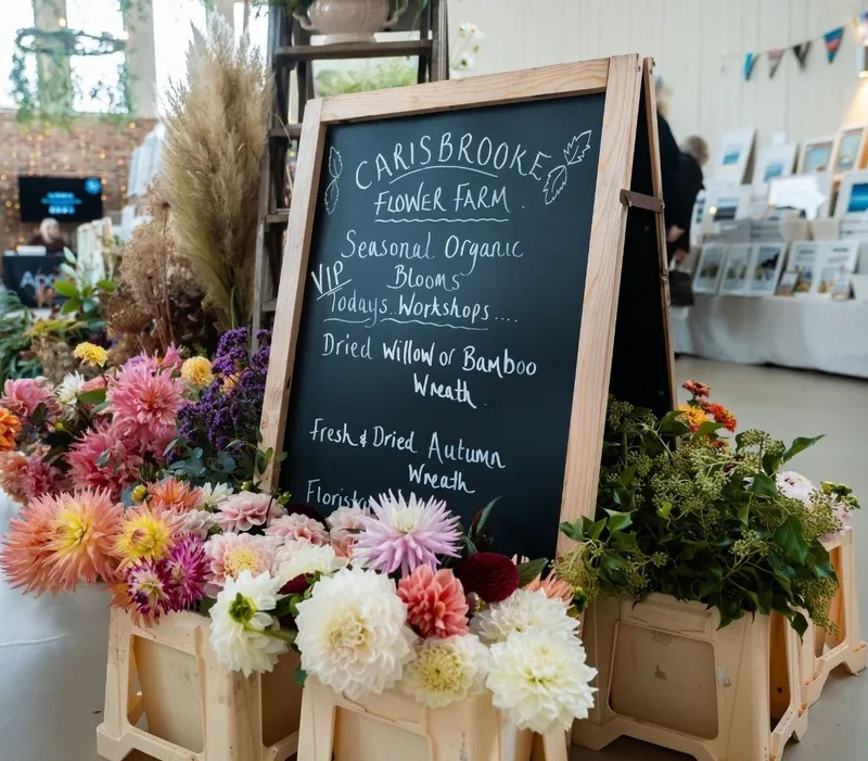 Chalkboard sign for Carisbrooke Flower Farm surrounded by colourful seasonal blooms at an interiors show