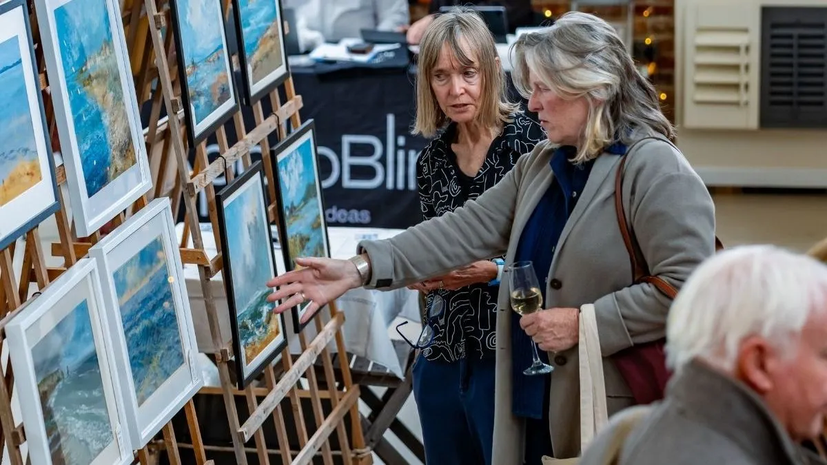Visitors viewing framed coastal artwork displayed on easels at an interiors show