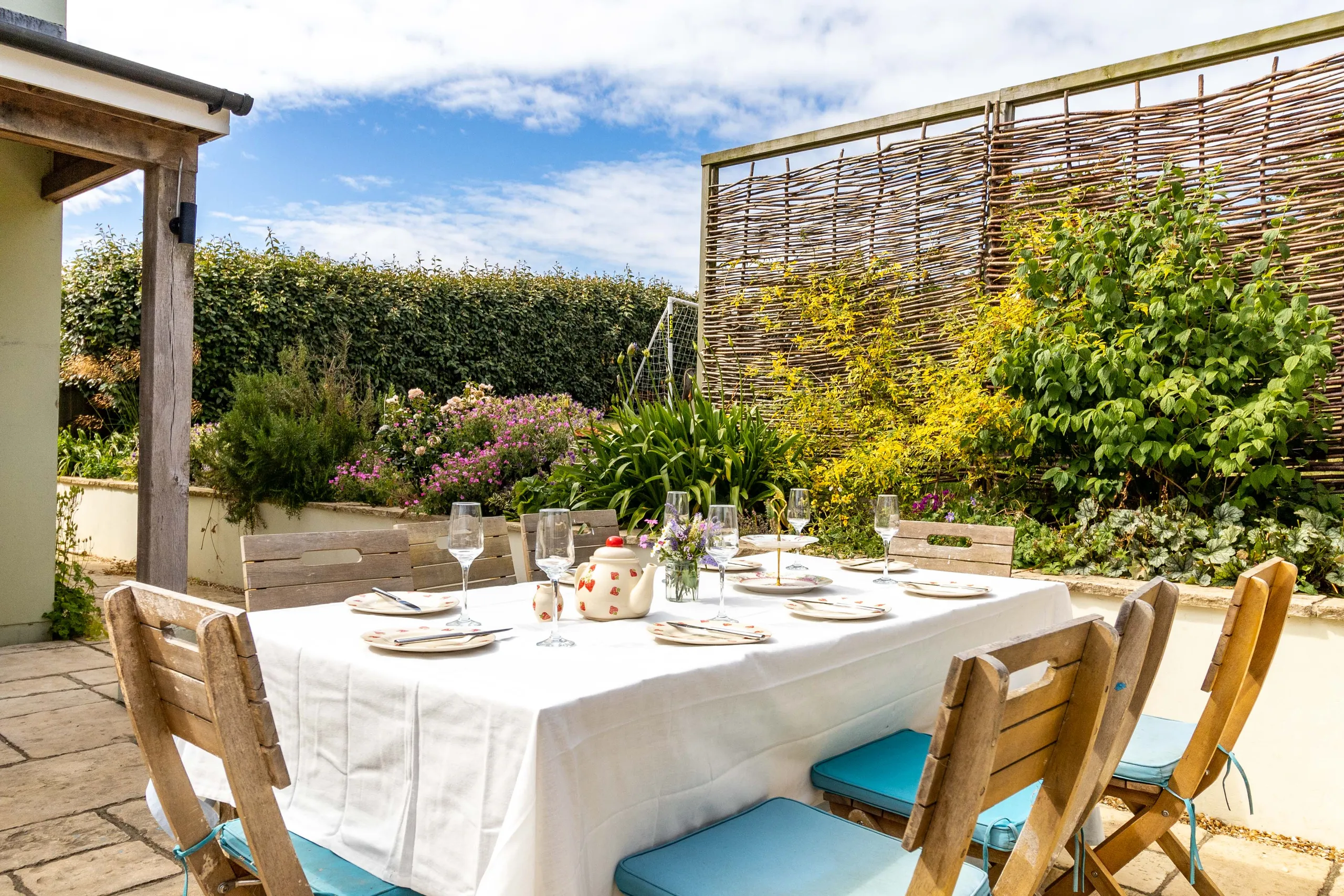 Outdoor patio dining table set with white tablecloth, plates and wine glasses in a sunny garden