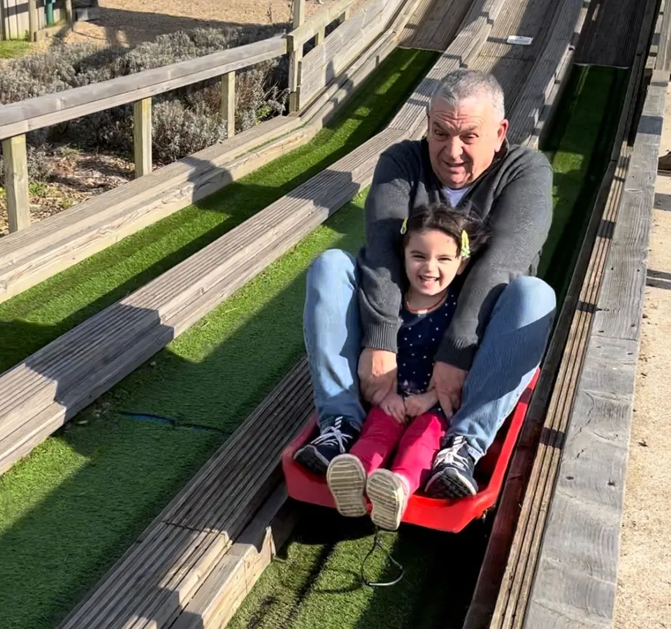 An older man and a young girl riding a red sledge down the slide at Tapnell Farm Park.