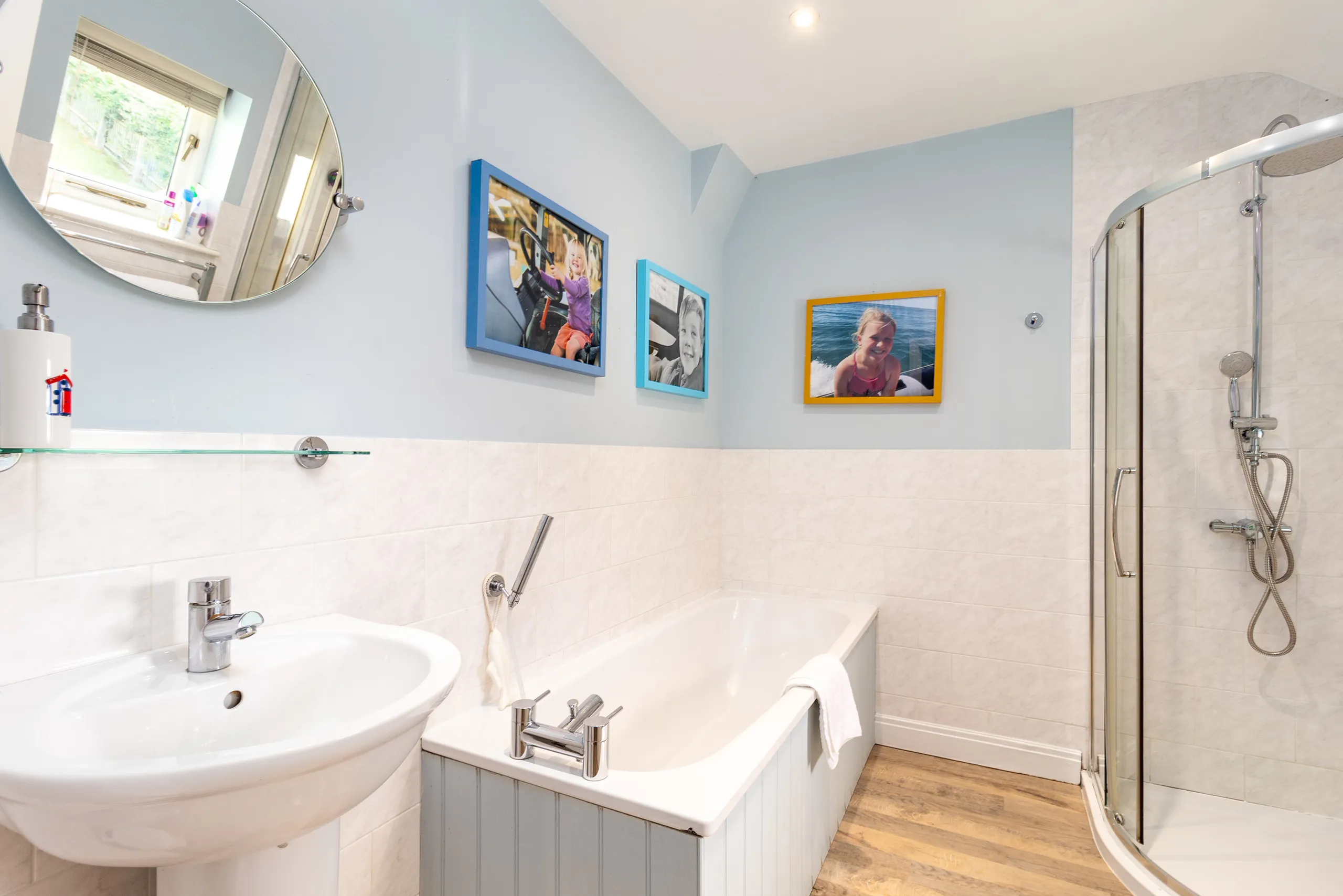 Bright bathroom with bath, pedestal sink, round mirror and curved glass shower enclosure