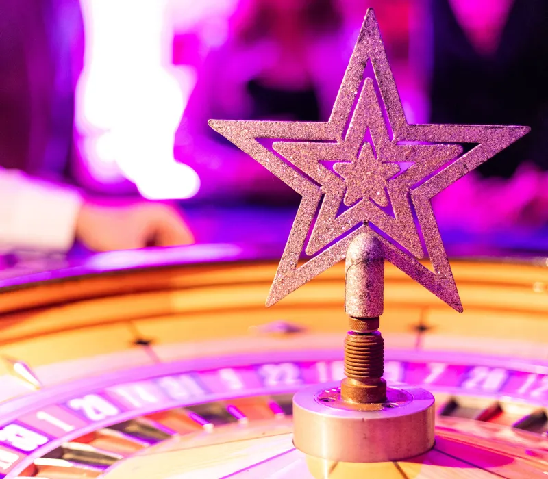 Glittery star roulette marker in sharp focus at a Christmas party, with guests blurred in pink and purple lighting behind.