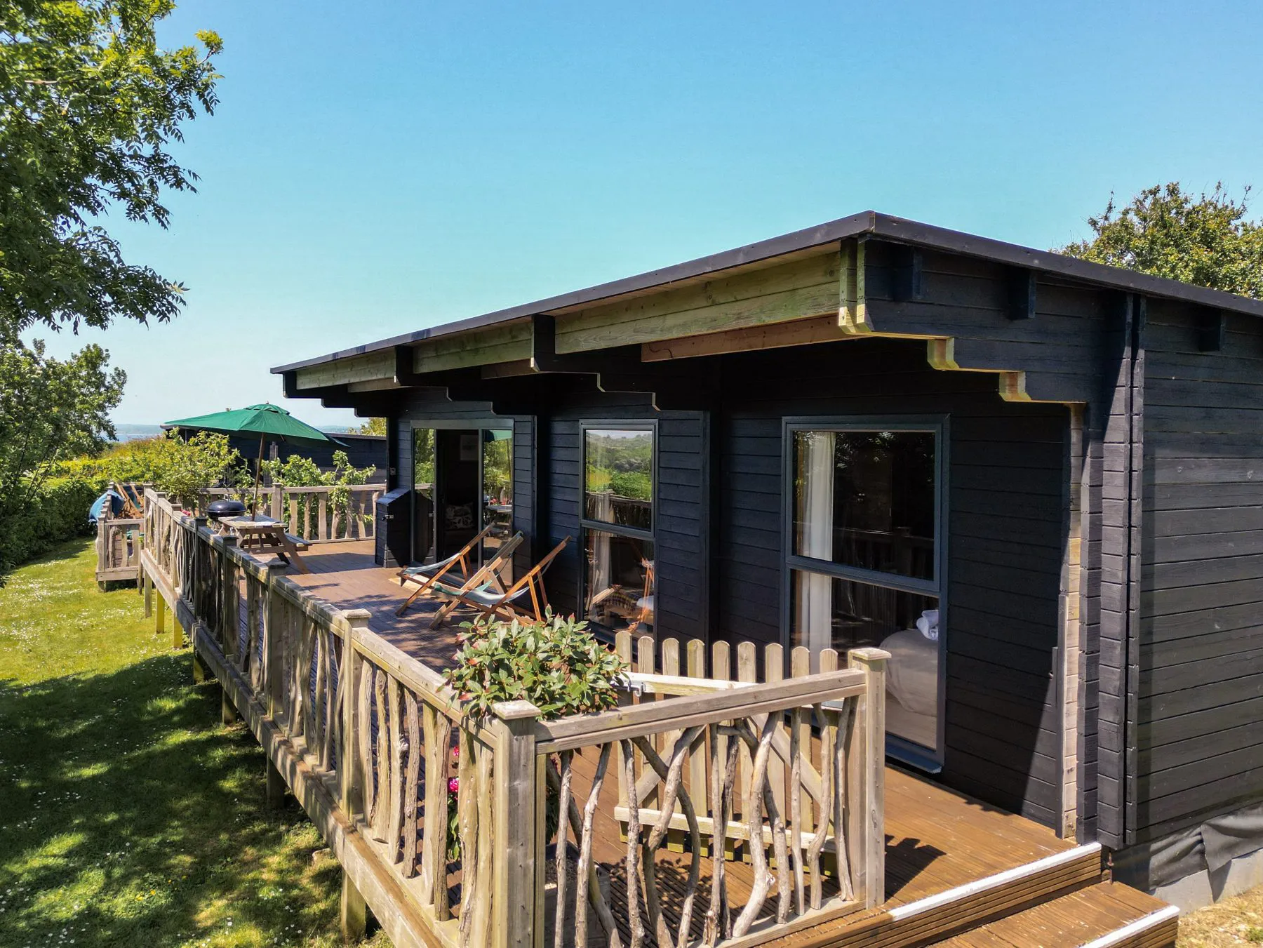 Wood cabin with large deck surrounded by greenery on a sunny day