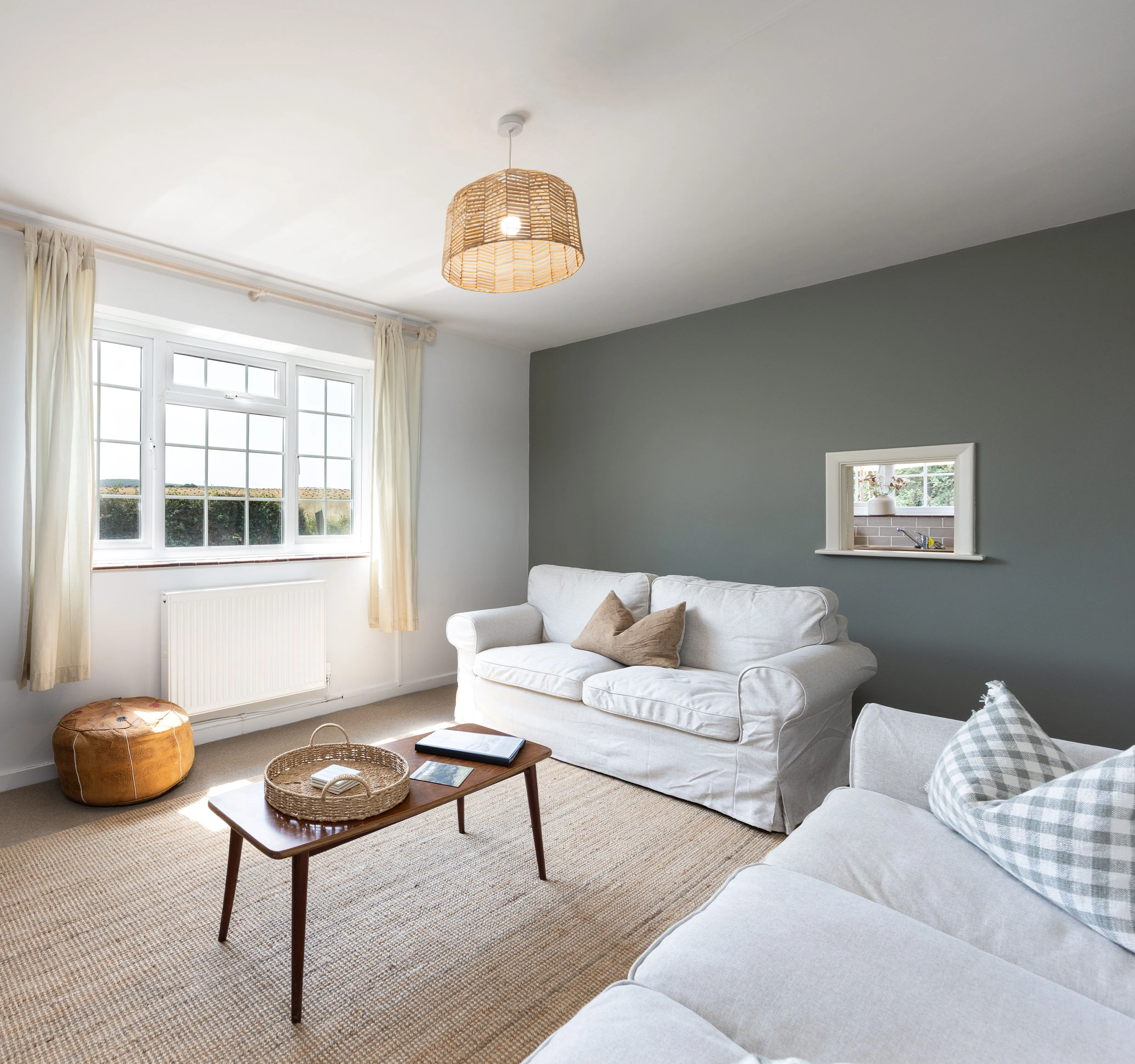 Bright, cosy cottage living room with white sofas, a wooden coffee table and a large window.