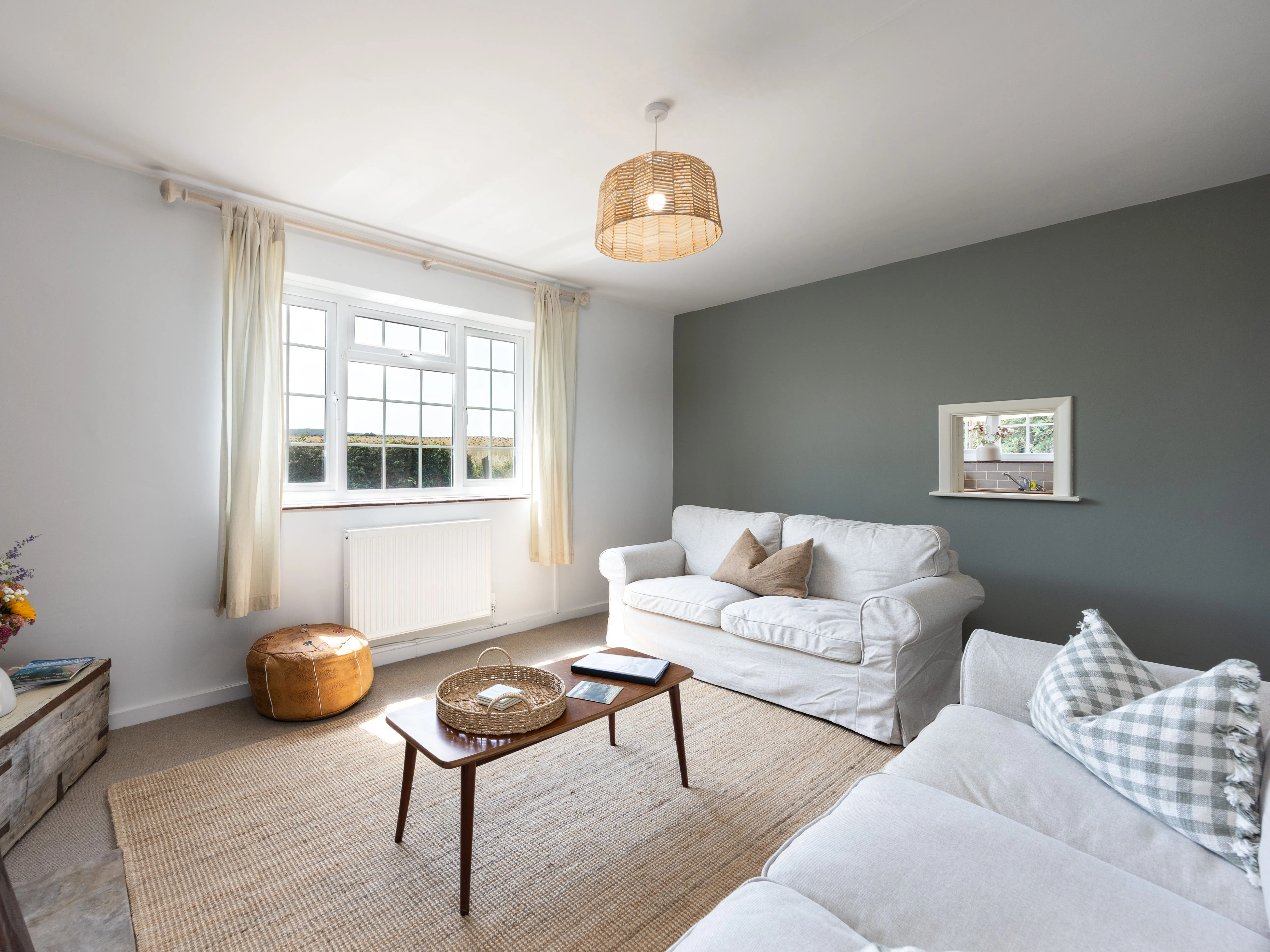 Bright, cosy cottage living room with white sofas, a wooden coffee table and a large window.