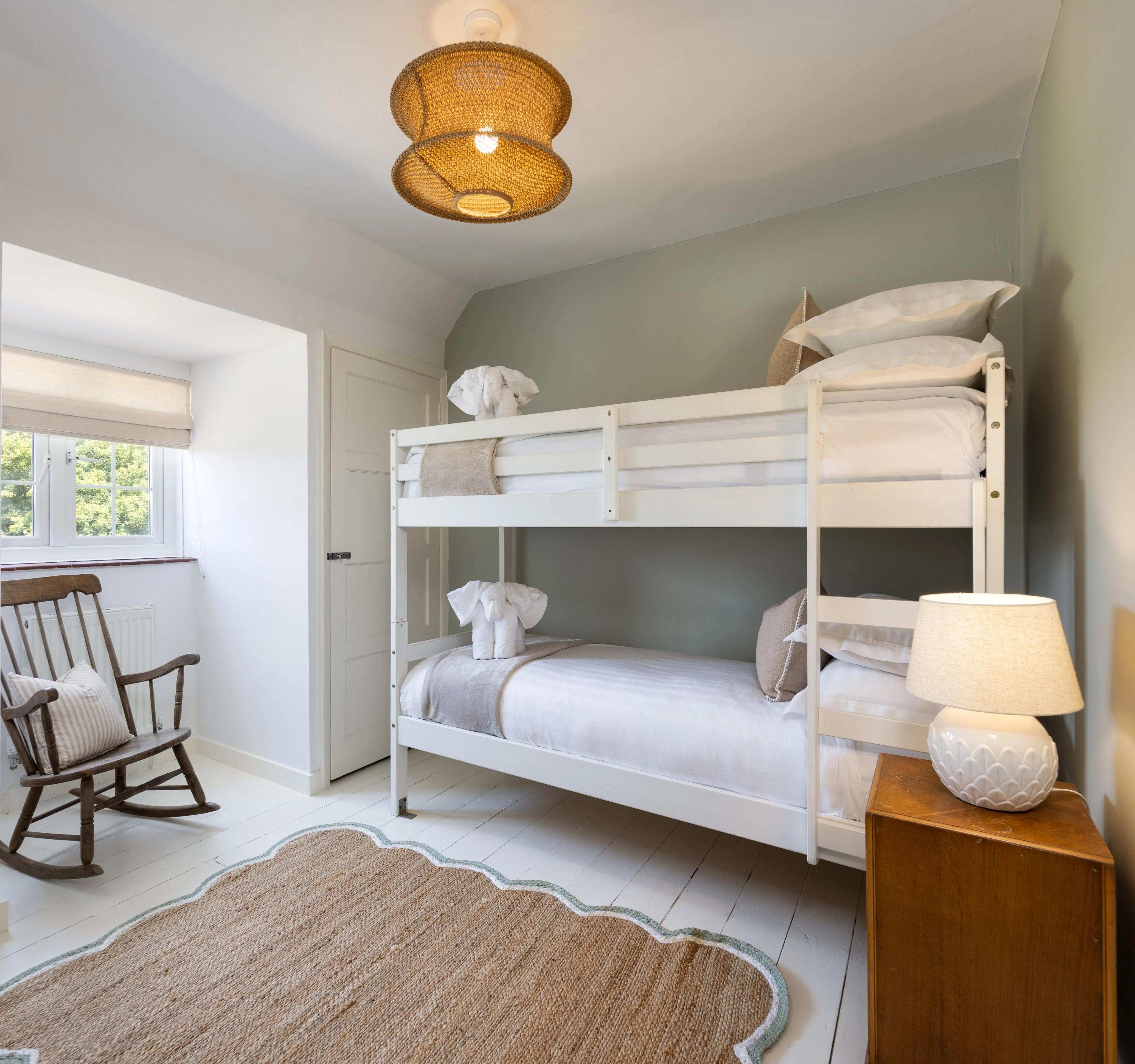 Cosy children's bedroom with white bunk beds, rocking chair and woven ceiling light