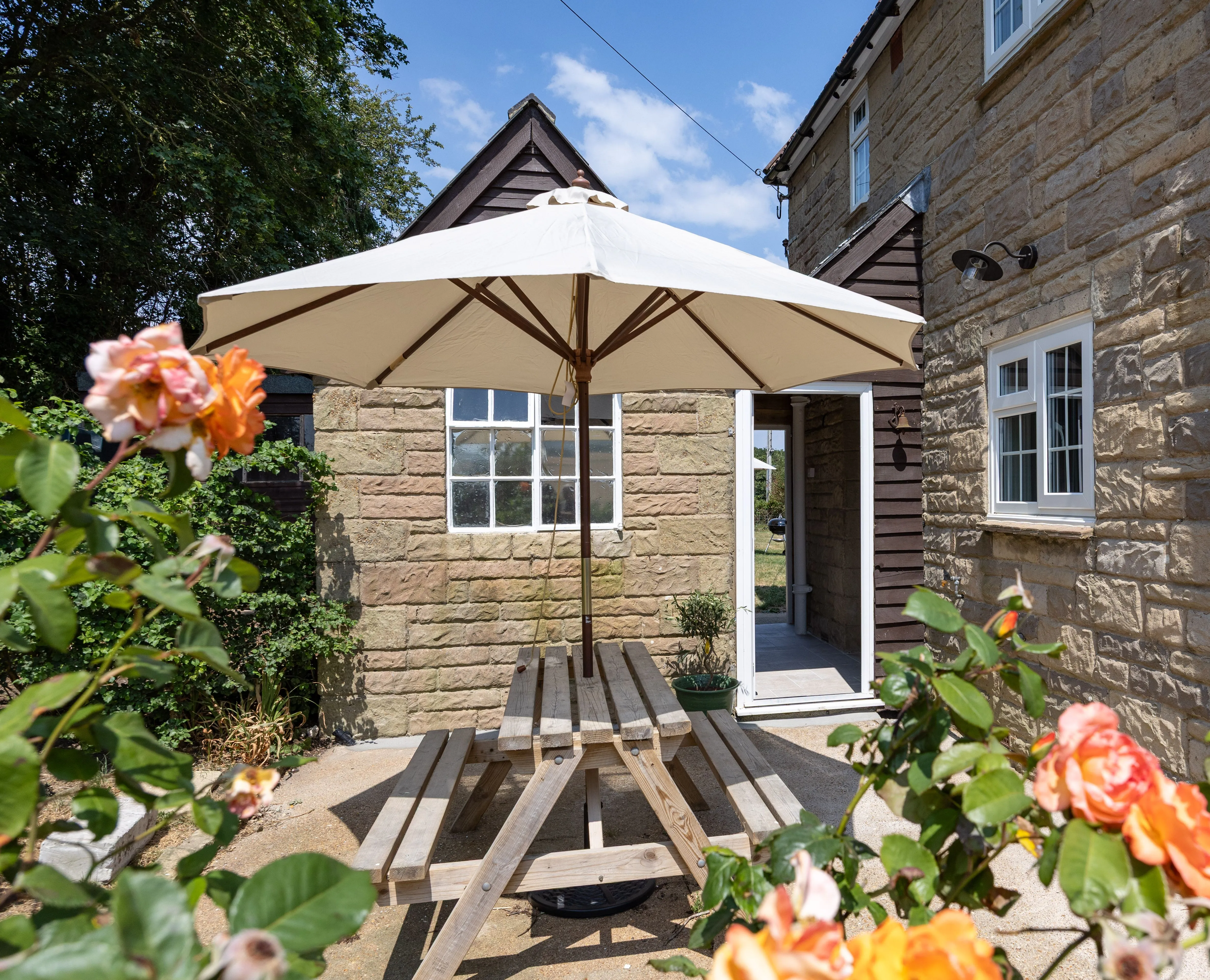 Stone cottage patio with a picnic table, parasol and blooming roses