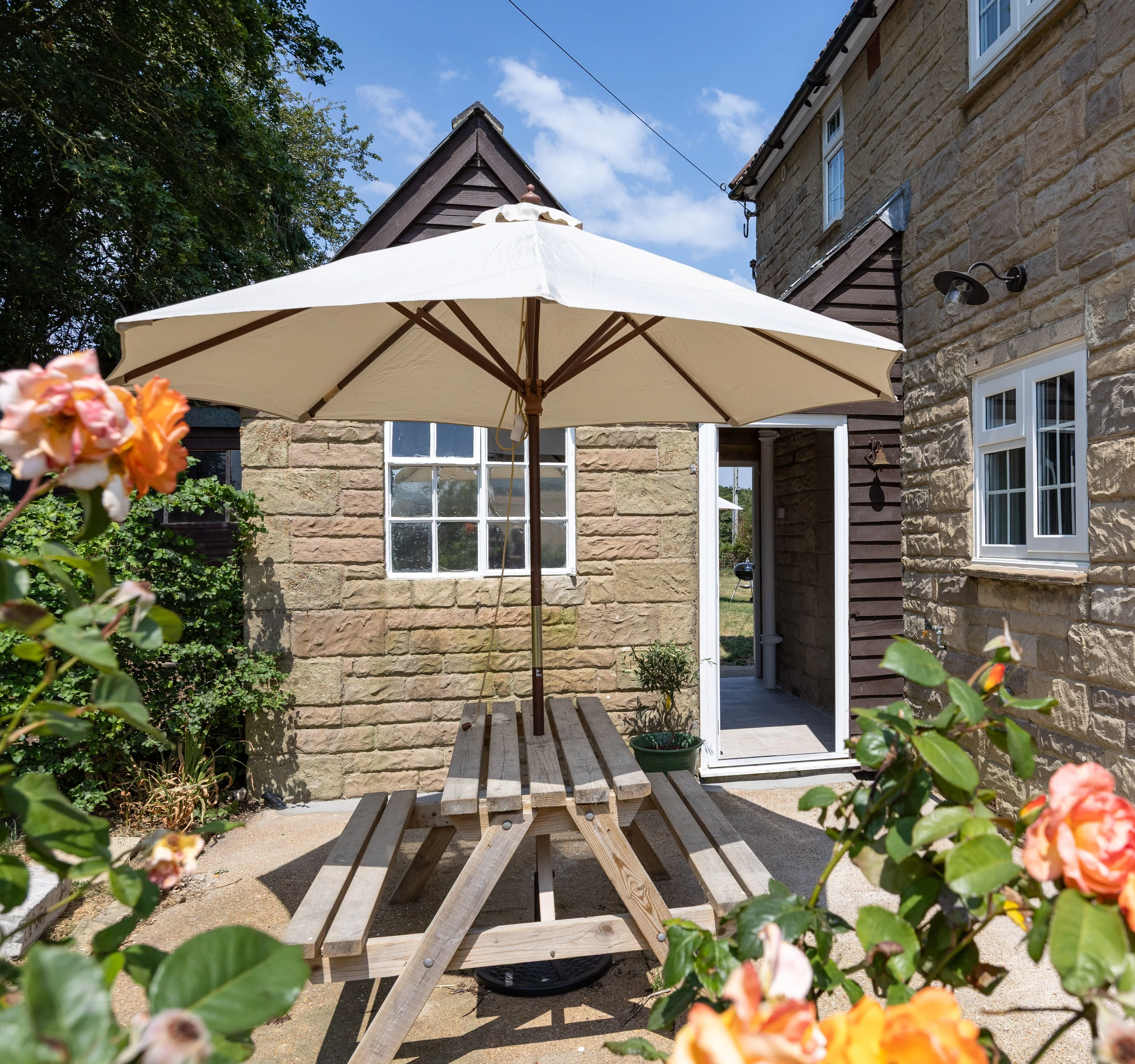 Stone cottage patio with a picnic table, parasol and blooming roses