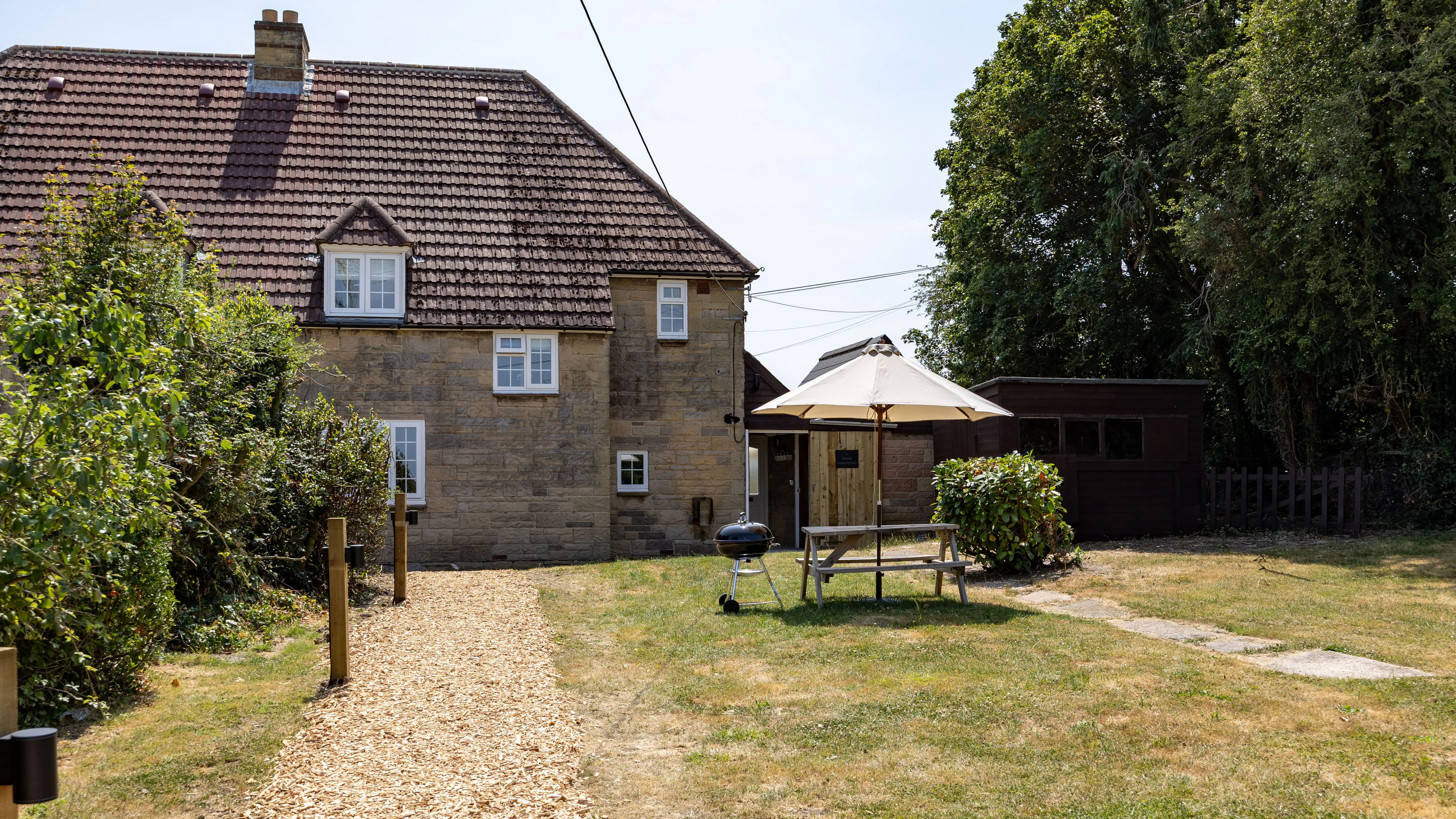 Stone cottage garden with picnic bench, parasol and barbecue