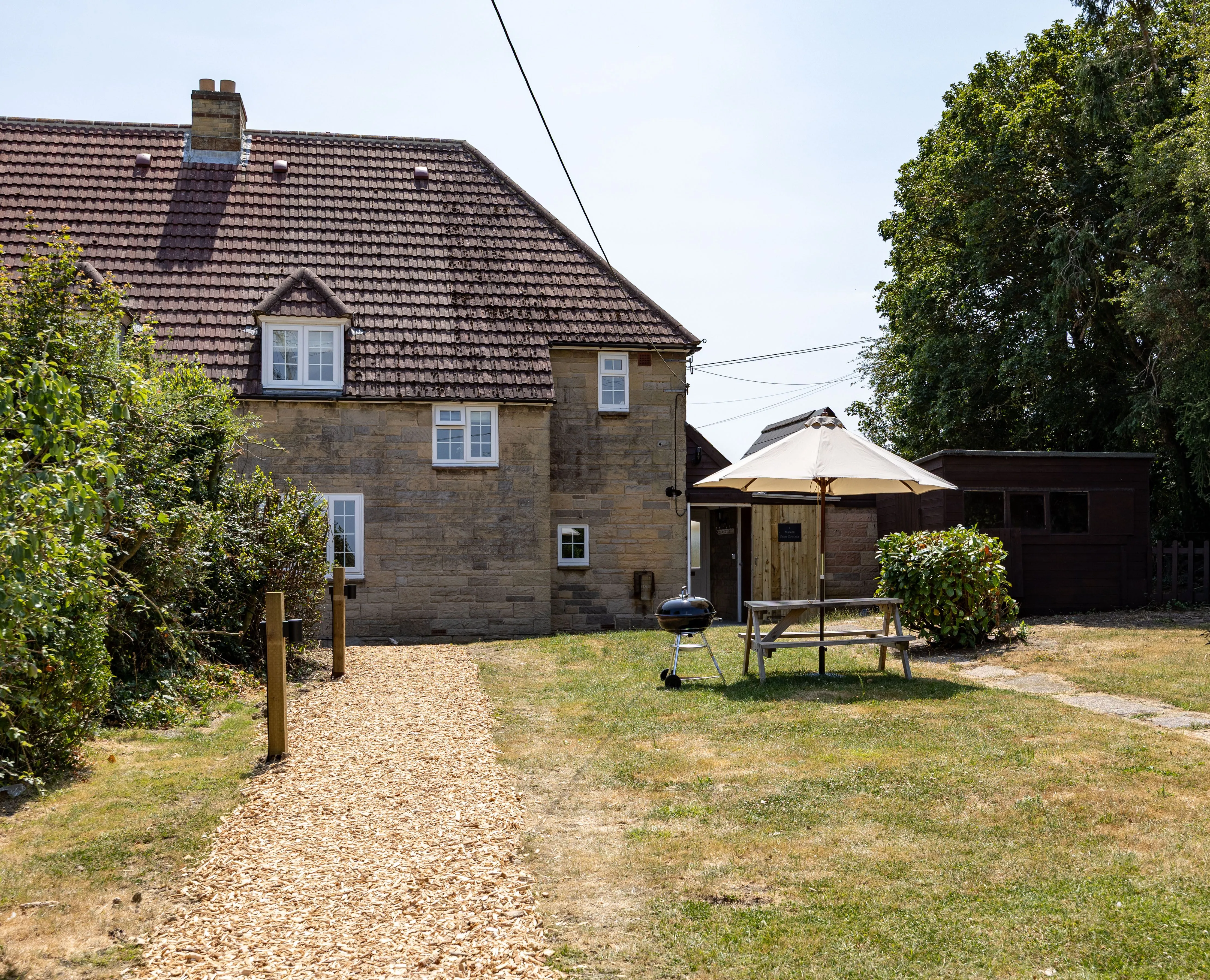 Stone cottage garden with picnic bench, parasol and barbecue