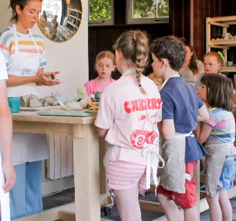 Children and adults gathered around a table during a pottery workshop.