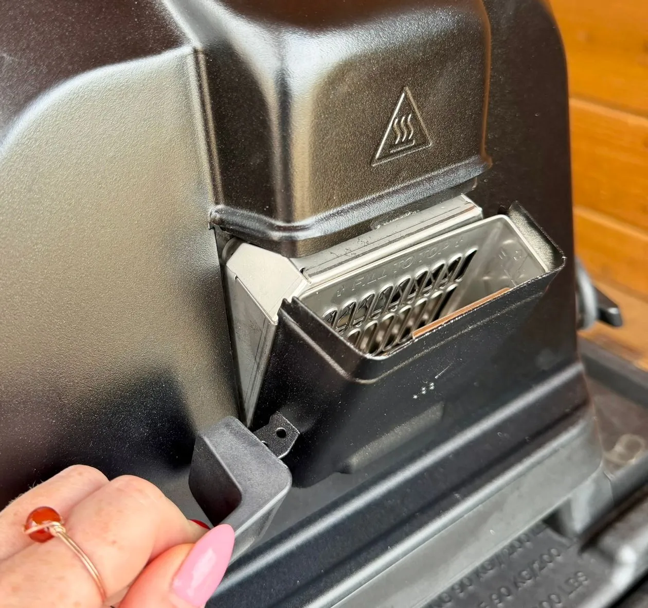 Close-up of a hand opening the ash drawer on a black pellet stove.