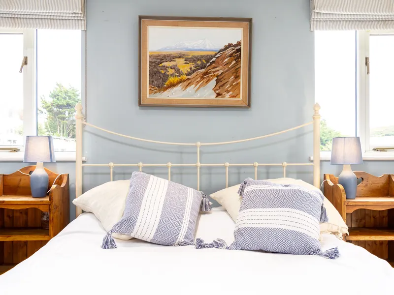 Bright bedroom with white metal bed, blue walls, patterned cushions and bedside lamps by two windows