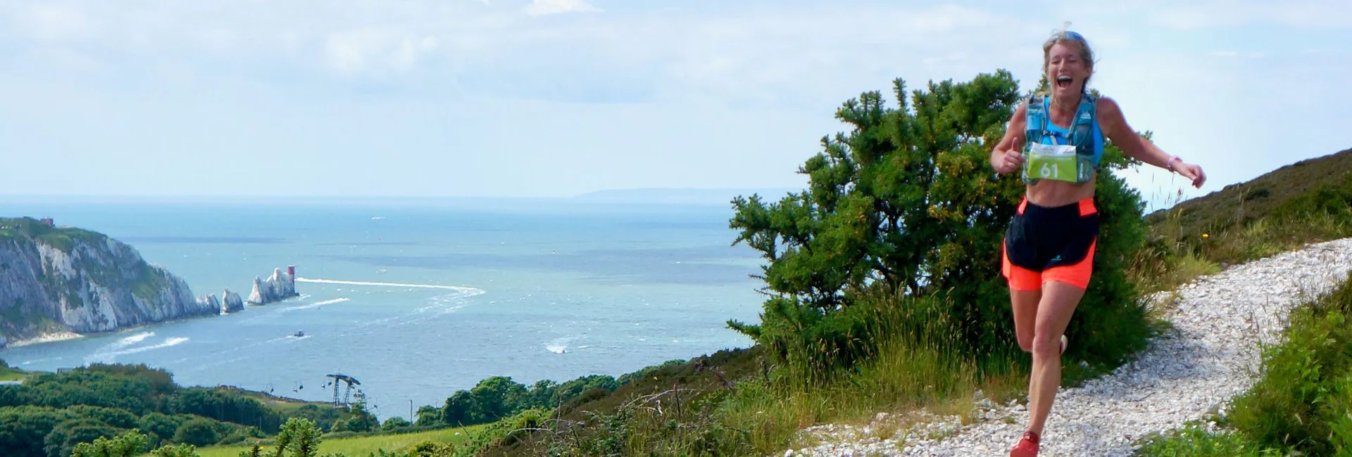 Female trail runner on a chalky coastal path overlooking the sea and cliffs under a blue sky.
