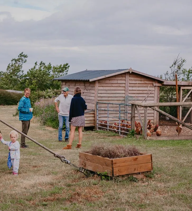 Adults and a young child gathered beside a wooden chicken coop in a rural garden
