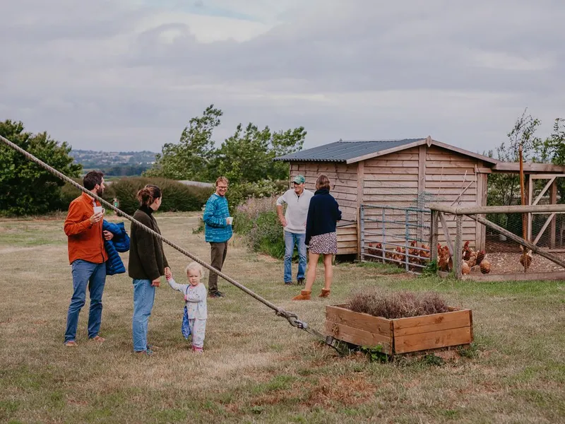 Adults and a young child gathered beside a wooden chicken coop in a rural garden