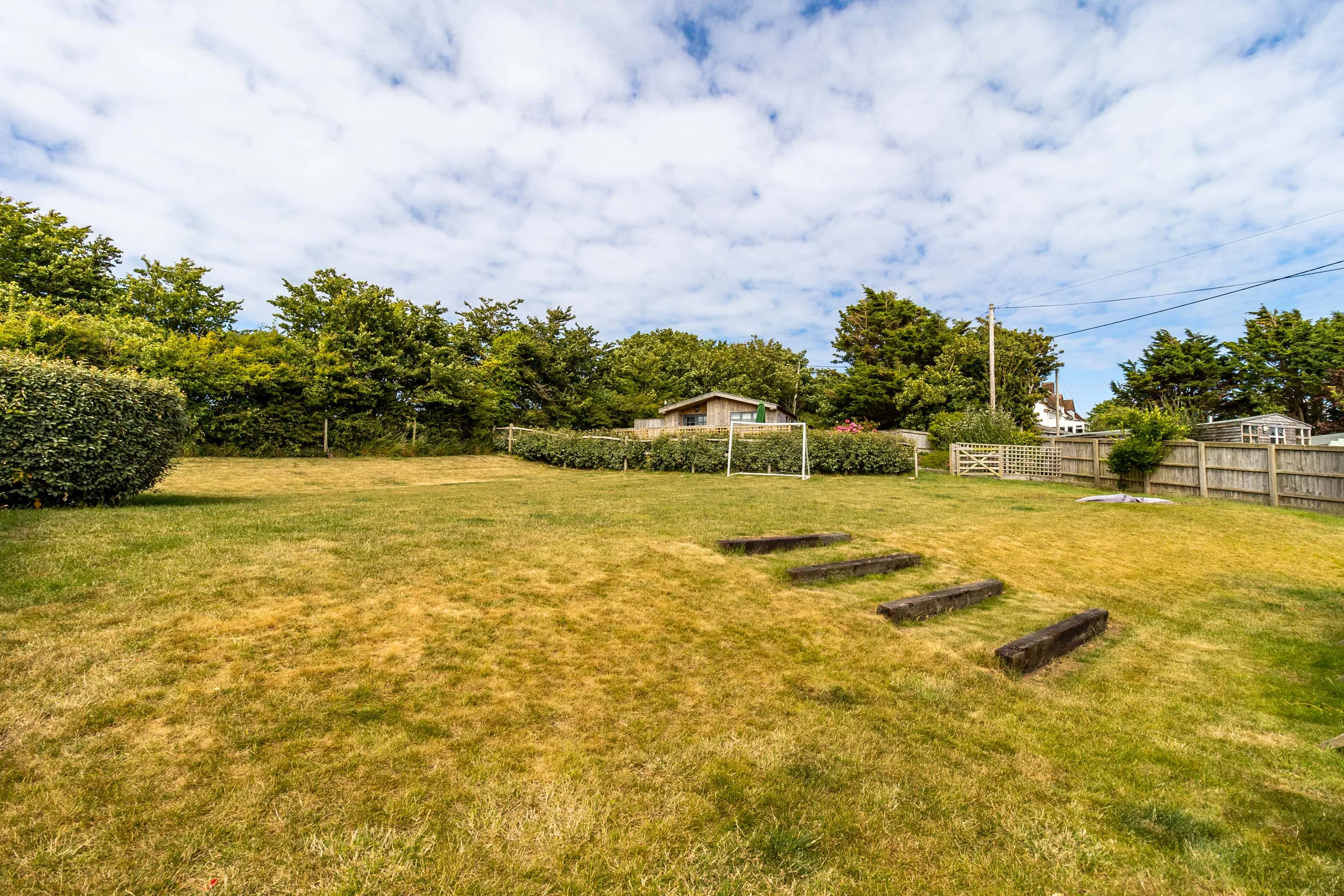 Large grassy garden with a football goal, timber steps and fenced boundaries under a partly cloudy sky