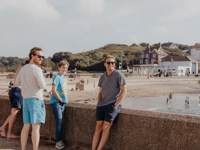 Three people standing by a seaside promenade wall overlooking a beach and coastal village.