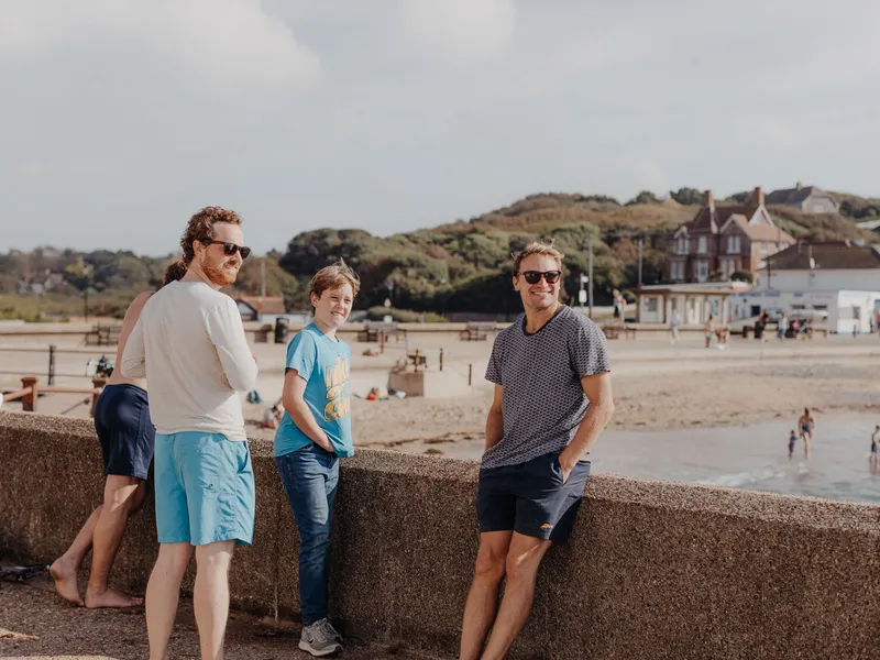 Three people standing by a seaside promenade wall overlooking a beach and coastal village.