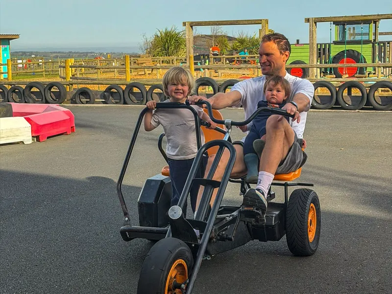 Man and two young children riding a pedal go-kart at an outdoor farm play area